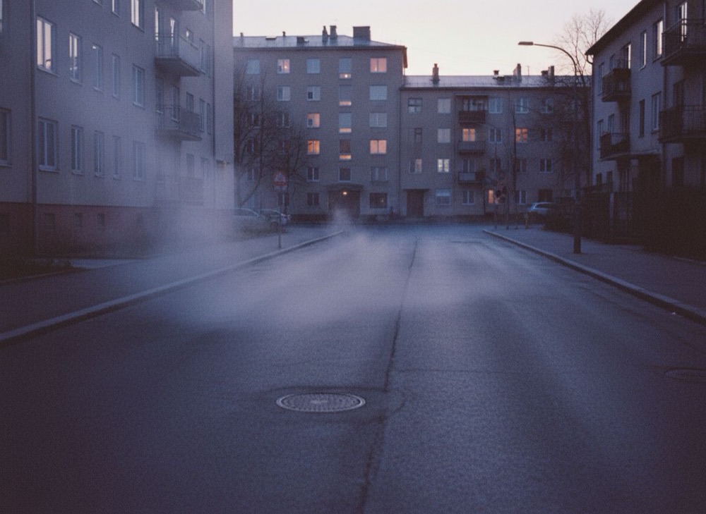 A city street before dawn, steam rising, a few lit windows above